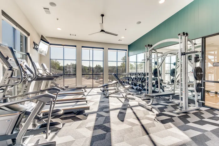 Modern fitness center with state-of-the-art treadmills and weightlifting equipment, illuminated by large windows and stylish lighting.