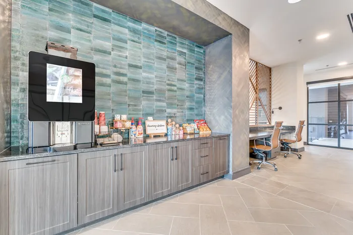 Modern apartment amenities featuring a sleek coffee station with snacks and cozy workspace with stylish chairs, perfect for relaxation and productivity.