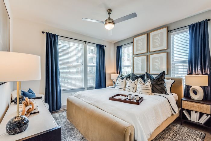 Inviting bedroom with elegant decor, featuring a plush bed, stylish lamps, and modern artwork, bathed in natural light from large windows.