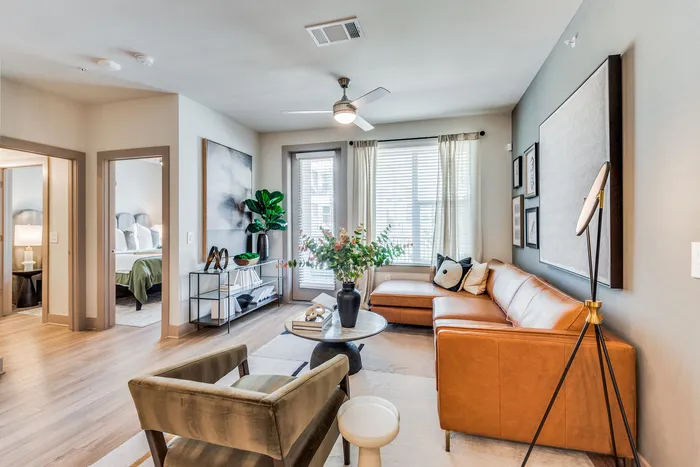 Modern living room with sleek leather couch, stylish decor, large windows, and adjacent cozy bedroom.