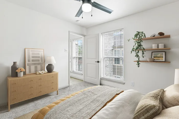 Bedroom with large window, floating shelf with plant, wooden dresser, ceiling fan, bed with tab bedding.