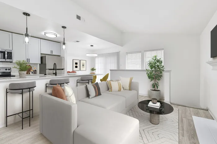 Living room with large sectional white couch with circular coffee table, kitchen bar with bar stools, pendant lighting, and stainless appliances.