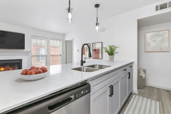 Kitchen with pendant lighting, white quartz counters, undermount sink, pendant lighting, wall art, living room in background with wall mounted TV.