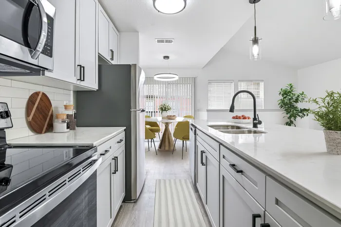 Kitchen with quartz counters with stainless appliances, pendant lighting, undermount since with gooseneck faucet. Dining table with chairs and glass sliding door.