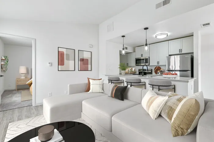 Large sectional white couch, black circular coffee table, kitchen bar with grey barstools, stainless appliances, and pendant lighting.