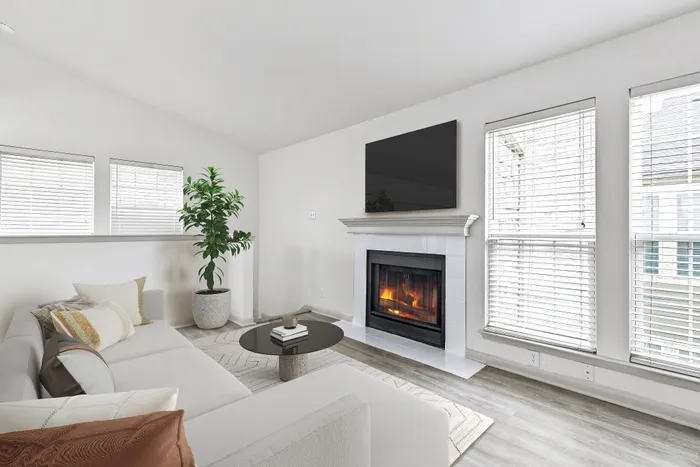 Large sectional white couch, multiple large windowns, circular coffee table, fire place, and wall mounted TV.