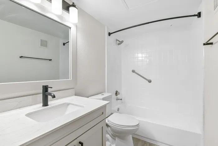 Bathrooom with vanity mirror and lighting, sink with quartz counters, shower with railnfall head nad curvered shower rod.