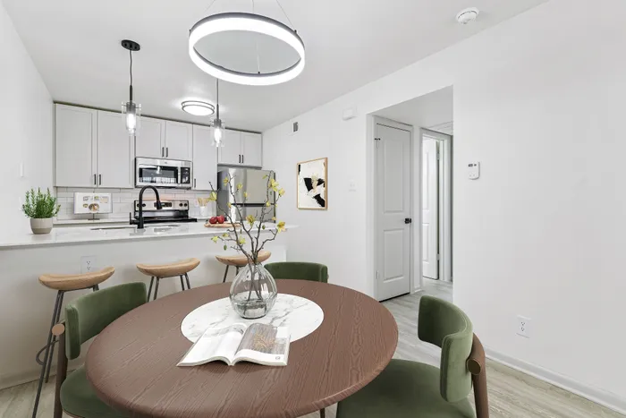 Wooden dining table with green chairs, kitchen with bar, wooden bar stools, white quartz counter, with pendant lighting.