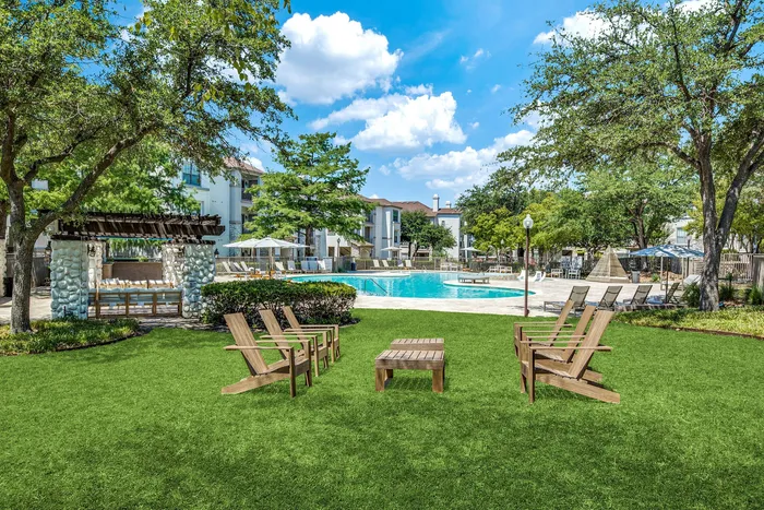 Luxurious outdoor area featuring a sparkling pool, comfortable lounge chairs, and lush green lawn under a bright blue sky.