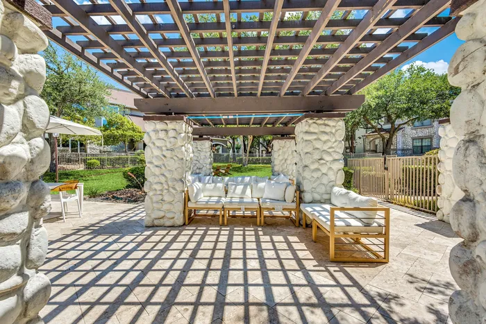 Inviting outdoor patio with cozy seating under a stylish pergola, surrounded by lush greenery and stone pillars.