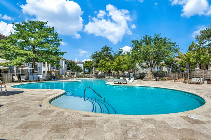 Luxurious apartment community featuring a sparkling outdoor pool surrounded by lush greenery and elegant lounge chairs.