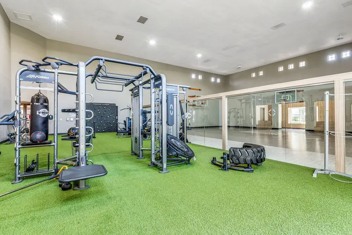 Spacious gym with modern fitness equipment and indoor basketball court, featuring vibrant green flooring and ample natural light.