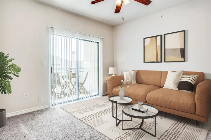 Bright and inviting living room with a modern tan sofa, elegant decor, and large sliding glass doors leading to a sunny balcony, perfect for relaxation and entertaining.