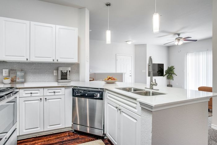 Bright modern kitchen with sleek appliances, pristine white cabinets, and a stylish breakfast bar. Inviting open-concept layout with a cozy living area and abundant natural light.