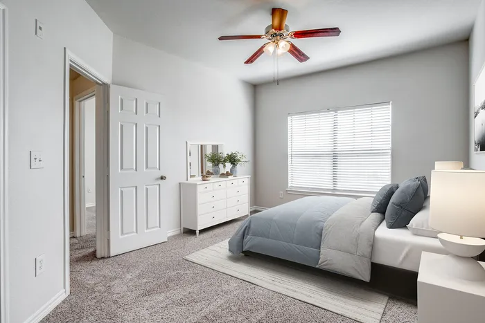 Bright and airy bedroom featuring a comfortable bed with elegant bedding, stylish ceiling fan, modern dresser with mirror, and abundant natural light through large window.