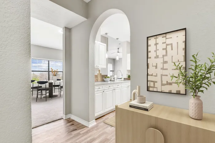 Elegant open-concept space featuring a stylish archway, bright kitchen with white cabinetry, and a cozy dining area with large windows.