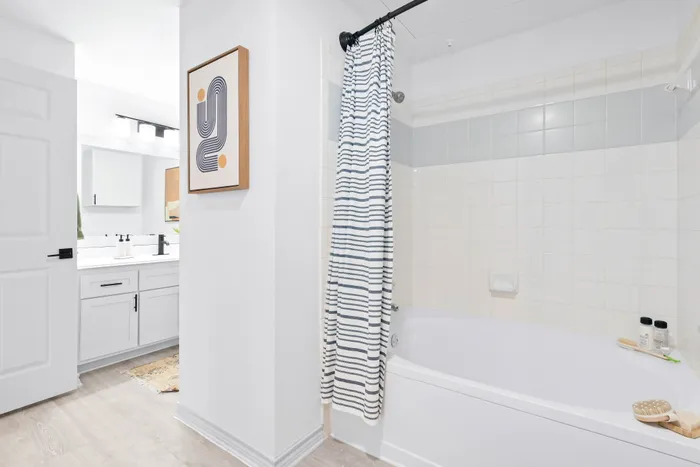 Bright modern bathroom featuring a sleek bathtub with striped shower curtain, elegant vanity with black fixtures, and stylish wall art.