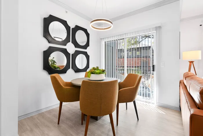 Bright dining area with chic circular mirror decor, modern round table, and stylish mustard chairs, bathed in natural light from sleek glass doors.