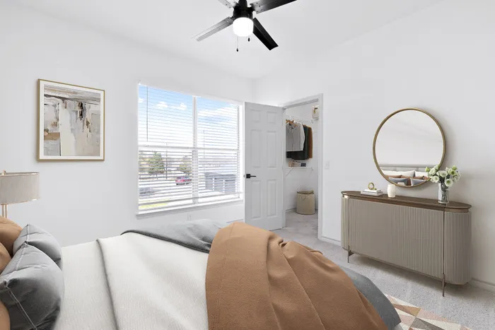 Bright and inviting bedroom with modern decor, featuring a cozy bed, large window with blinds, and a stylish mirrored dresser. The room includes a spacious walk-in closet for ample storage.