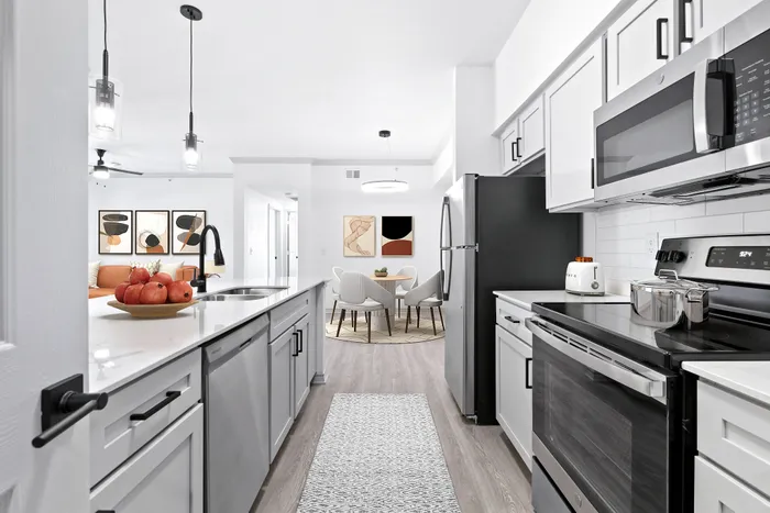 Modern open-concept kitchen and dining area featuring sleek appliances, elegant pendant lighting, and a stylish art display.