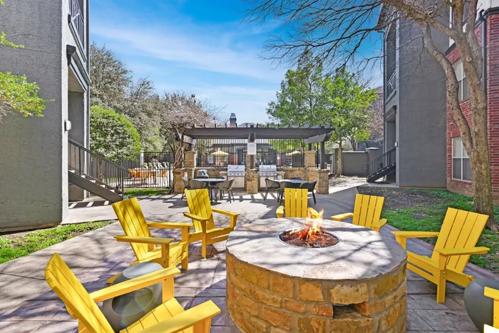 Brick fire pit with six yellow chairs, blue skies and trees