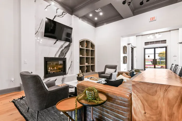 Interior leasing office with wall mounted tv, chairs, leather couch, and fireplace