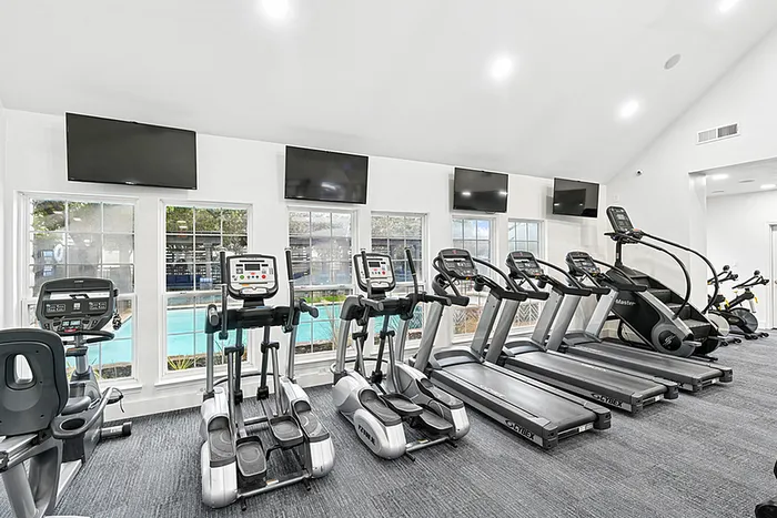 Fitness center with TVs mounted on the wall and fitness equipment facing windows overlooking the pool.