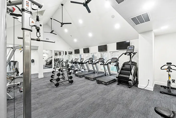 Fitness center with TVs mounted on the wall and fitness equipment facing windows overlooking the pool.