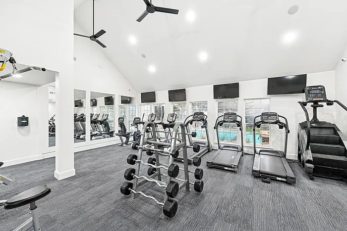 Fitness center with TVs mounted on the wall and fitness equipment facing windows overlooking the pool.