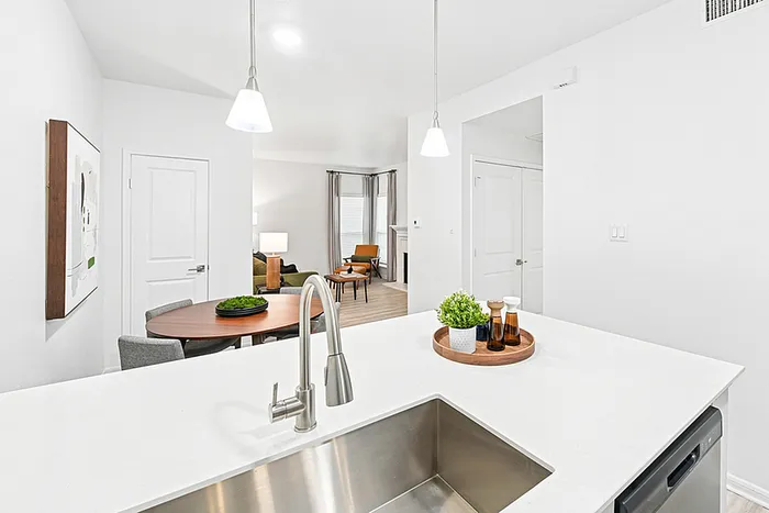 Kitchen with white quartz counters, pendant lighting, undermounted sink, dining table, wall art.