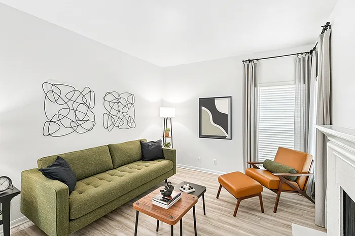 Living room with sofa, wooden table, lounge chair, large windows, wall art, and lamp.