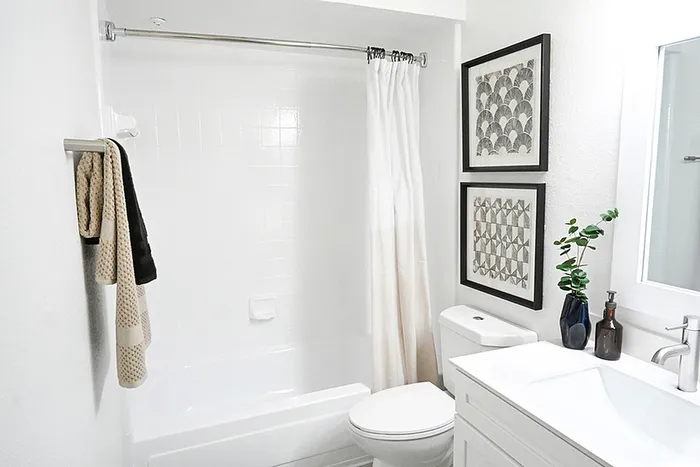 Bathroom with quartz counters, wall art, mirror, towel rack, and curved rod.