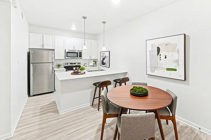 Dining area with round table, kitchen bar with quartz counters, pendant lighting, wall art, and stainless appliances.