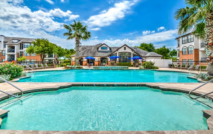 Luxurious apartment complex featuring a pristine swimming pool surrounded by vibrant palm trees and elegant outdoor seating areas under a clear blue sky.