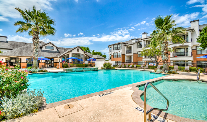 Luxurious apartment complex showcasing a refreshing pool with lounge chairs, surrounded by lush palm trees and vibrant gardens.