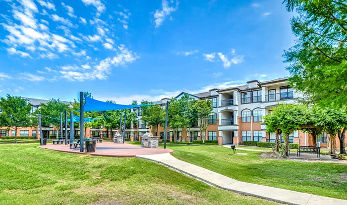 Inviting apartment complex surrounded by lush greenery and outdoor gathering areas under a bright blue sky.