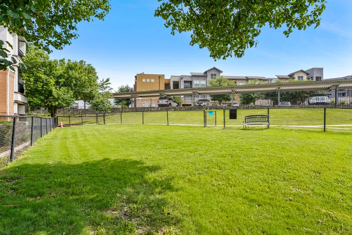 Bright and spacious outdoor area with lush green grass, perfect for relaxation and leisure, set against modern apartment buildings and shaded parking in the background.