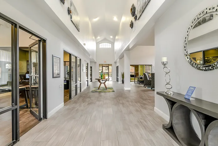 Elegant and bright lobby area with modern decor, featuring a large circular mirror, stylish table, and natural light streaming in through tall windows.