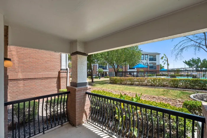 Charming apartment patio with a refreshing view of the lush green courtyard and inviting community pool area.