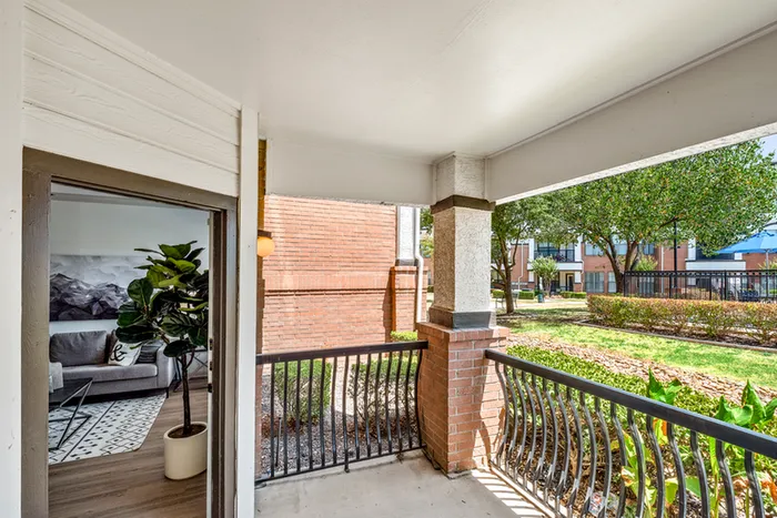 Inviting apartment balcony overlooking lush green courtyard with modern interior glimpses.