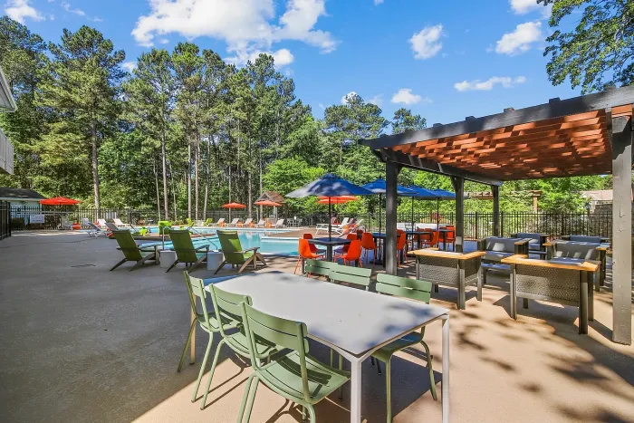 Inviting outdoor swimming pool area with vibrant loungers, shaded seating, and lush green surroundings, ideal for relaxation and social gatherings.