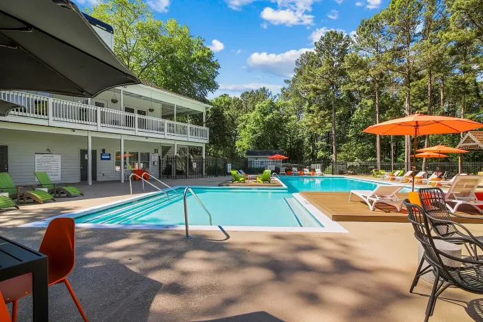 Inviting outdoor swimming pool area with lounge chairs, vibrant orange umbrellas, and surrounded by a serene forest setting, perfect for relaxation and entertainment.