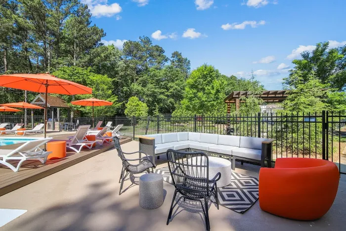 Chic outdoor lounge area by the pool with vibrant orange umbrellas, modern sun loungers, and lush green surroundings.