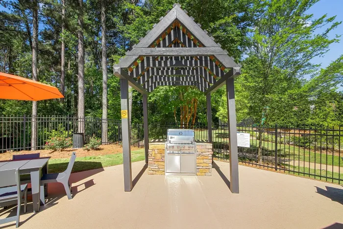 Outdoor grill area with a stylish pergola, modern grill, and cozy seating, surrounded by lush greenery.