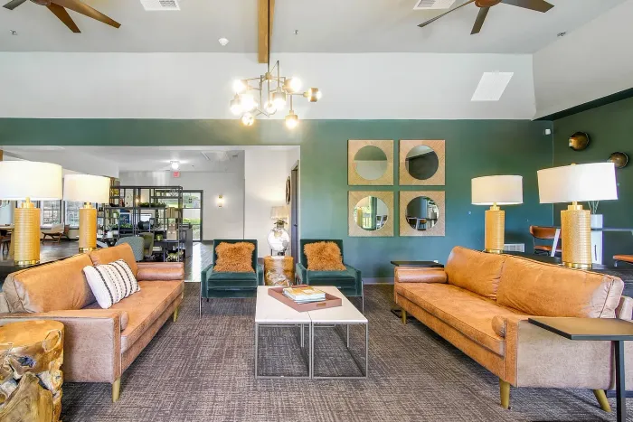 Elegant resident clubhouse living room with plush leather sofas, modern lighting, and stylish decor featuring geometric mirrors and plush seating.