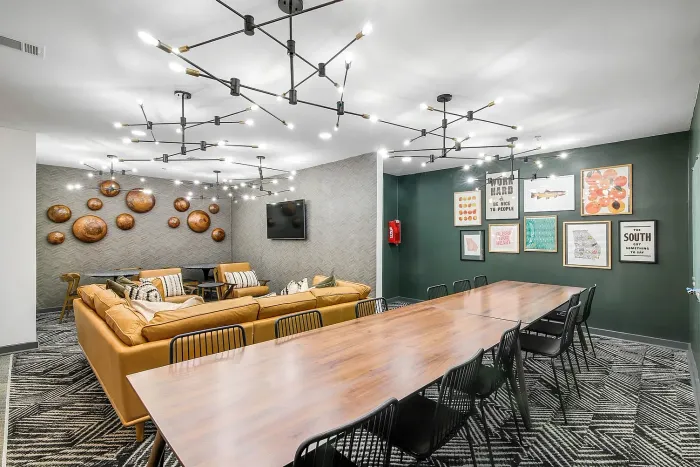 Chic and modern resident lounge area with elegant lighting, inviting mustard-colored sectional sofas, and a stylish dining table, perfect for social gatherings and relaxation.