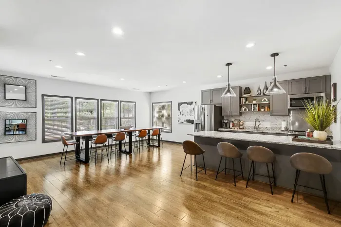 Elegant open-concept resident clubroom kitchen and dining area with stylish gray cabinetry, sleek pendant lights, and bar seating, perfect for entertaining.