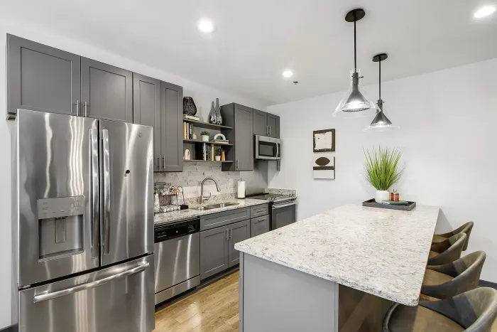 Modern resident clubhouse kitchen with sleek stainless steel appliances, elegant gray cabinetry, and a chic marble countertop island with stylish pendant lighting.