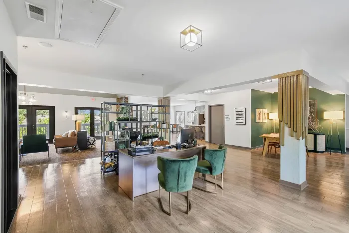 Elegant leasing office featuring modern decor, open seating with plush green chairs, and abundant natural light highlighting the stylish design.