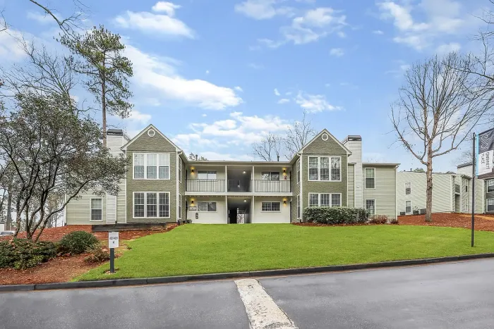 Charming apartment community with a modern exterior, surrounded by lush greenery and blue skies, offering a welcoming atmosphere.